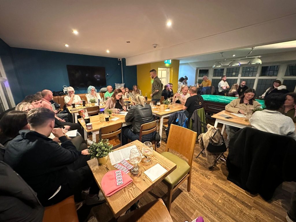 A busy charity quiz night with groups of people seated around tables in a pub.