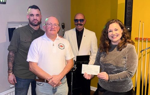 Four people standing together at a fundraising event, with a woman holding a cheque for Headway Shropshire.
