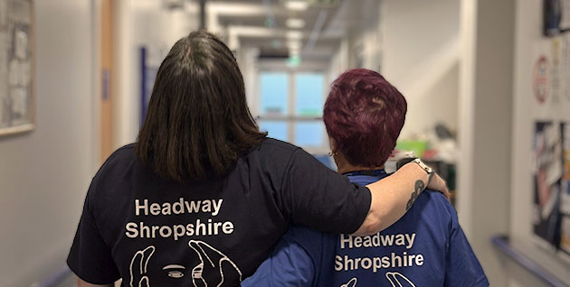 One to one support service - two Headway Shropshire employees walking down a corridor, one with their arm around the other's shoulders in support.