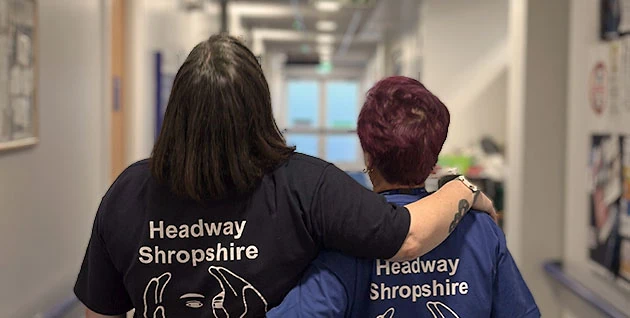 One to one support service - two Headway Shropshire employees walking down a corridor, one with their arm around the other's shoulders in support.
