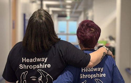 One to one support service - two Headway Shropshire employees walking down a corridor, one with their arm around the other's shoulders in support.