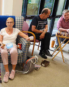 Three people sitting together in a lounge area, with a chess board set up on a small table.