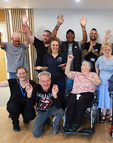 Headway Shropshire clients and staff posing together indoors, smiling and raising their hands.
